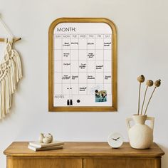 a wooden cabinet with a calendar hanging on the wall next to a potted plant