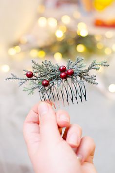 a person is holding a comb with berries and pine needles on it in front of a christmas tree