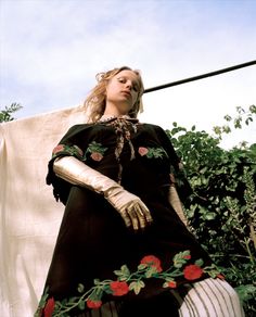 a woman in a black dress with red roses on her chest and arms, standing next to a clothes line