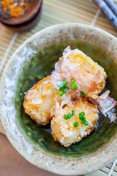 some food in a green bowl on a table with chopsticks and other items