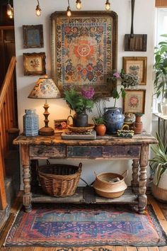 an old table with baskets and plants on it in front of a wall hanging tapestry