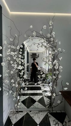 a man standing in front of a mirror with white flowers on the wall and black and white checkered floor