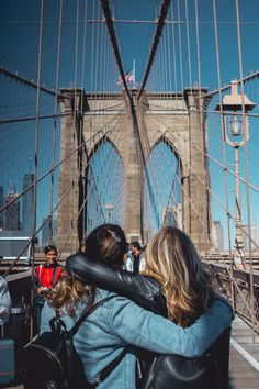 two women hugging each other in front of the brooklyn bridge with people standing on it