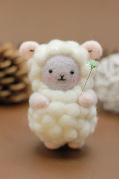 a small stuffed sheep holding a flower on a table next to some pinecones