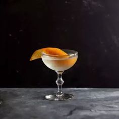 an orange garnish in a martini glass on a dark table with two glasses