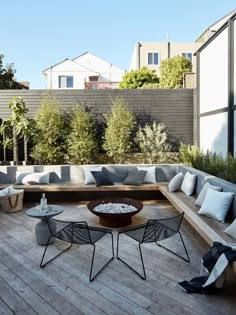 an outdoor seating area with wooden floors and white pillows on the couches, surrounded by greenery