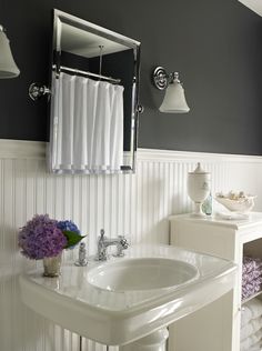 a white sink sitting under a bathroom mirror next to a counter with flowers on it