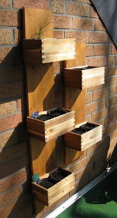 some plants are growing in wooden boxes on the side of a brick wall and green grass