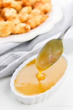 a spoon full of sauce being poured into a bowl with tater tots in the background