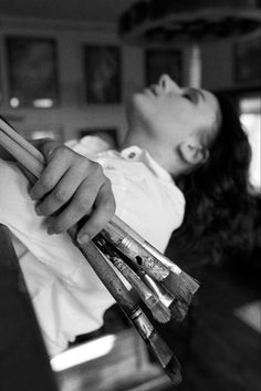 black and white photograph of a woman with her eyes closed holding several paintbrushes