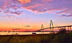 the sun is setting behind a bridge over water with trees and bushes in front of it