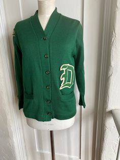 This is a green Albion Knit virgin wool varsity knit cardigan circa 50s/60's. In excellent condition, with no holes snags or stains. Patch on arm is GLS and there is a large "D" patch on front above pockets. There is a faded name printed on label "Tircuit" There is no size label but my guess is small.  Measurements are: Shoulders: 17" Pit to pit: 19" Length: 25" Sleeve length: 21" cuffed, 23" uncuffed Vintage Sweater For College In Winter, Vintage Winter Sweater For College, Retro Cotton Cardigan For College, Retro Long Sleeve Cardigan For College, Vintage College Sweater For Fall, Vintage Sweater For College In Fall, Vintage College Sweater For Winter, Vintage Fall Sweater For College, Green Varsity Sweater For Winter