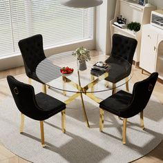 a round glass table with black chairs and a white rug in front of the window