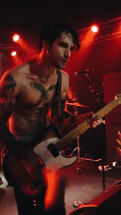 a shirtless man holding a guitar on stage