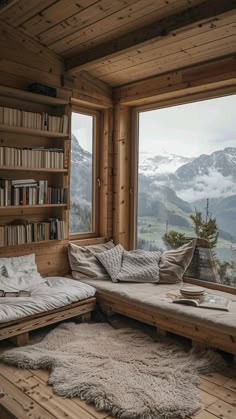 a room with a couch, bookshelf and window overlooking the mountain range in winter