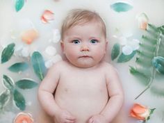 a baby is sitting in a bathtub with flowers around it and looking at the camera