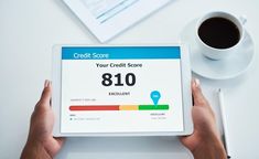 a person holding a tablet with a credit score displayed on the screen next to a cup of coffee