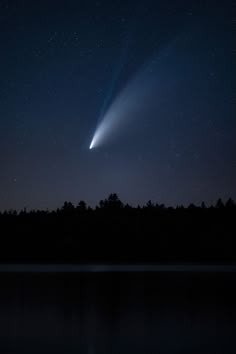 a comet is seen in the night sky over water and trees with stars above it