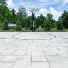 an empty basketball court in the middle of a park with trees and bushes around it