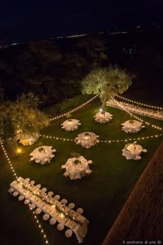 an aerial view of tables and chairs set up with fairy lights strung across the lawn