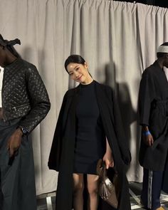 three people standing next to each other in front of a white curtain and wearing black clothing