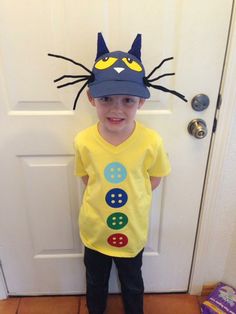 a young boy wearing a yellow shirt with a cat on it's head standing in front of a door