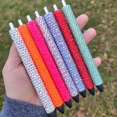 a hand holding five different colored pens in it's palm and the other one is made out of plastic beads