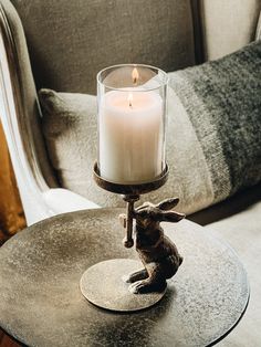 a lit candle sitting on top of a metal table next to a gray chair and pillow