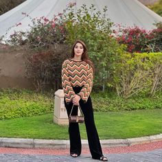 a woman standing in front of a white tent holding a brown and black handbag