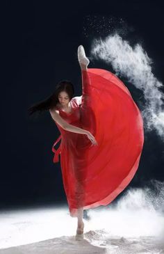 a woman in a red dress is dancing with her arms spread out and she has long black hair