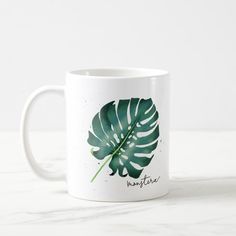 a white coffee mug with a large green leaf on the front and bottom of it