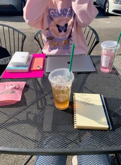 a person sitting at a table with a drink and notebooks on it, talking on the phone