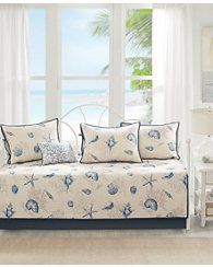 a white couch sitting in front of a window covered in blue and white pillows with seashells on them