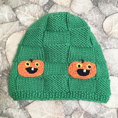 a green knitted hat with two orange bears on it's eyes and nose