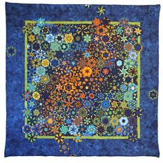 a blue quilt with colorful flowers and stars on the border is displayed in front of a white background