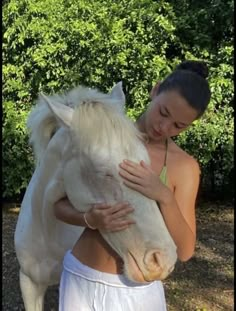 a woman is hugging a white horse outside