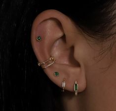 a close up of a person wearing ear piercings with green stones on their ears