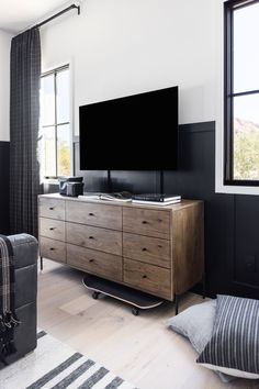 a flat screen tv sitting on top of a wooden dresser in a living room next to a window