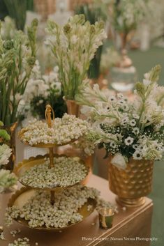 three tiered trays filled with white flowers and greenery on top of a table