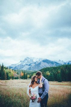 a bride and groom standing in the middle of a field with mountains in the background