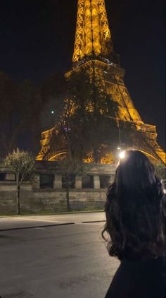 a woman standing in front of the eiffel tower at night