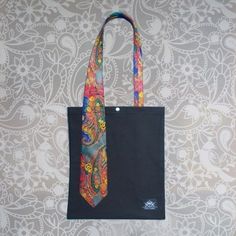 a black tote bag with a colorful tie hanging from it's front pocket