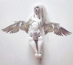 a white doll with wings sitting on top of a wall