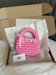 a pink purse sitting inside of a cardboard box on top of a bed next to a white tag