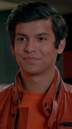 the young man is wearing an orange jacket and smiling at the camera with his eyes wide open