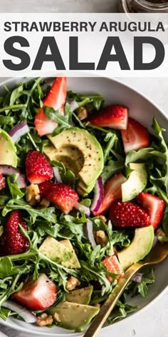 a salad with strawberries, avocado and spinach on top in a white bowl