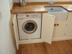 a washer sitting inside of a kitchen next to a sink and counter top on a wooden floor