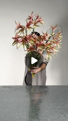 a man holding a vase filled with flowers on top of a metal table next to a white wall