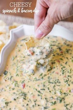 a hand dipping a tortilla chip into a bowl of cheese spinach and bacon dip