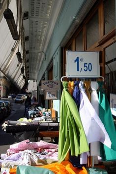 an outdoor market with cloths and clothing for sale on the street side, next to a sign that reads 1 50